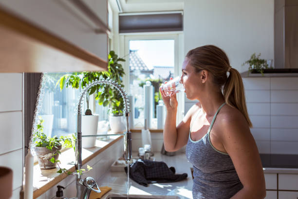 Femme qui boit un verre d'eau dans sa cuisine